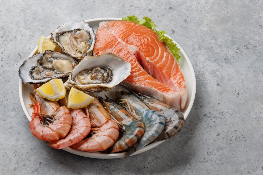 A plate of seafood featuring oysters, shrimp, and a slice of salmon with lemon wedges and lettuce.