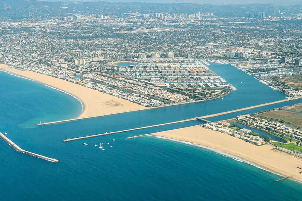 Aerial view of Marina del Rey with sandy beaches, blue water, marina channels, and surrounding cityscape.