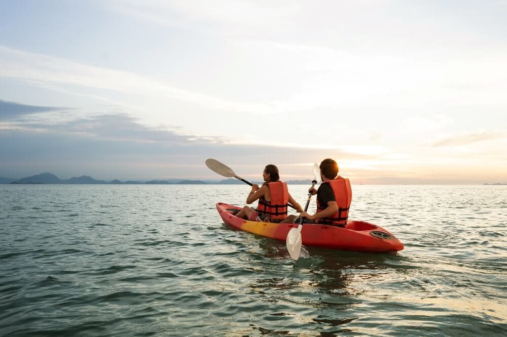 Two people kayaking together on calm ocean water during sunset.